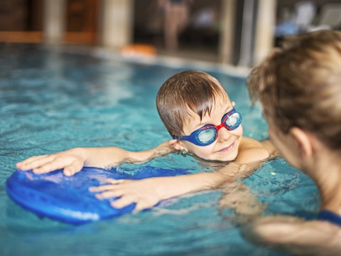 Boy using a kickboard to swim with lady helping him