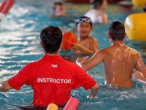 swimming instructor in a red top in a swimming pool with two boys playing