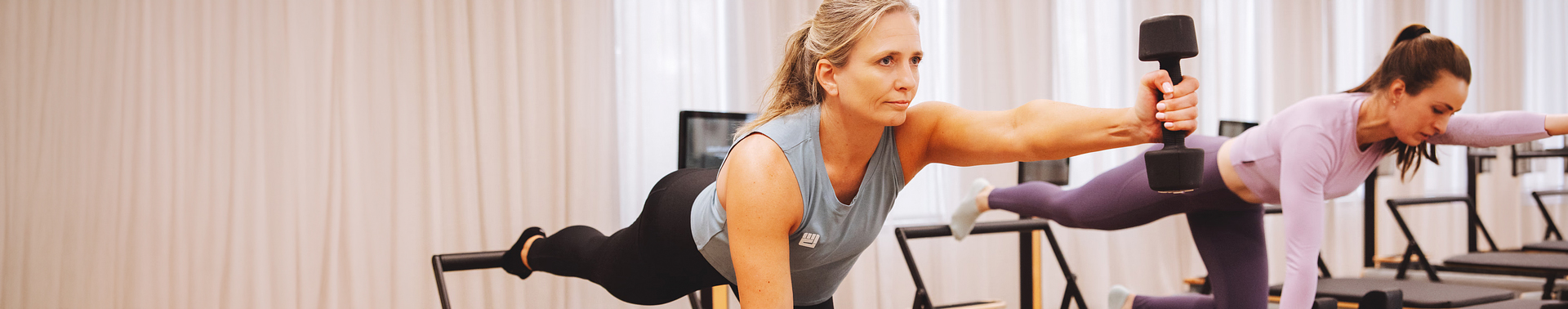 A lady on a reformer holding out a dumbbell